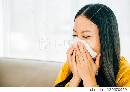 A woman at home holding a tissue experiencing symptoms like coughing and stuffy nose. Portrait of a patient dealing with illness. Snot and handkerchief in hand. 120670959
