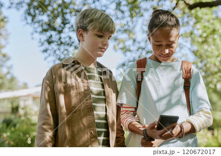 Medium shot of two ethnically diverse teen boys standing in botanical garden, reading information about plants on smartphone 120672017