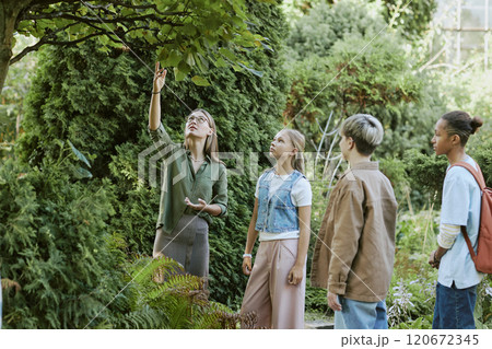 Young female teacher of biology showing trees to group of her teen students during outdoor lesson in local botanical garden Young female teacher of biology showing trees to group of her teen students during outdoor lesson in local botanical garden 120672345