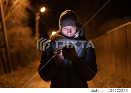 Couple holding hands while walking on a quiet road at night, illuminated by a streetlight, surrounded by bare trees and a serene atmosphere. 120672346