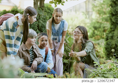 Young female specialist working in local botanical garden showing rare plants to group of teen students Young female specialist working in local botanical garden showing rare plants to group of teen students 120672347
