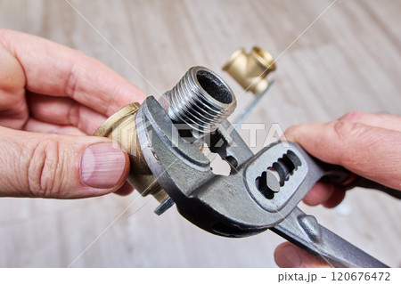 Plumber uses an adjustable wrench to tighten hexagonal nipple adapter into elbow fitting of mounting bracket. 120676472