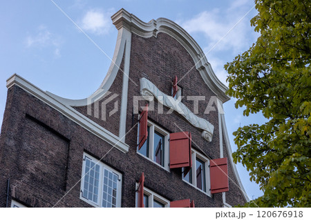 A charming Dutch building with red shutters, dated 1690, nestled on a cobblestone street. A bench and plants adorn the entrance, creating a cozy and historic ambiance. Dordrecht landscape. 120676918