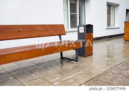 Wooden bench and trash bin with no smoking sign on a wet pavement. 120677446