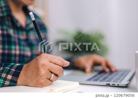 A woman hand holding a pencil while working at small office and using a laptop. Close up shot hands of freelancer use laptop working on desk of her this is a lifestyle of freelance or editor. A woman hand holding a pencil while working at small office and using a laptop. Close up shot hands of freelancer use laptop working on desk of her this is a lifestyle of freelance or editor. 120679056