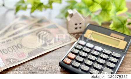 新1万円札3枚と家小物と計算機_茶色板背景 120679385