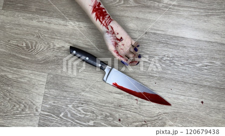 Crime scene with knife covered in blood and victim bloody hand on floor. Murder of girl with knife in domestic crime. Raising awareness about domestic violence and protecting lives of woman Crime scene with knife covered in blood and victim bloody hand on floor. Murder of girl with knife in domestic crime. Raising awareness about domestic violence and protecting lives of woman 120679438