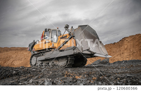 Yellow excavator in career moves overburden. Bulldozer working in an open pit. Bulldozer combs the ground, with the bright sun and nice blue sky in the background. Mining digger, mining machinery Yellow excavator in career moves overburden. Bulldozer working in an open pit. Bulldozer combs the ground, with the bright sun and nice blue sky in the background. Mining digger, mining machinery 120680366