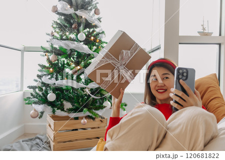 Happy red shirt woman making a video call holiday greeting with her friends and family showing the Christmas tree.  120681822