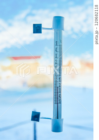 An outdoor thermometer is attached with adhesive tape to window glass outside, on scale of 20 degrees below zero Celsius. 120682118