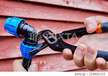 Adjustable plumbers wrench pliers for pipes are used to tighten compression clamp nut of elbow fitting for joint plastic pipes, red background. 120682125