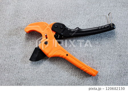 An orange and black pipe cutter lies on concrete surface. An orange and black pipe cutter lies on concrete surface. 120682130