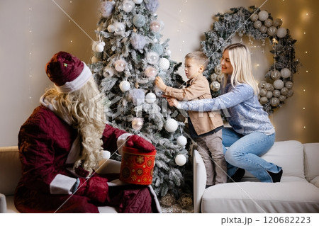 Santa claus watching mother and son decorating christmas tree Santa claus watching mother and son decorating christmas tree 120682223