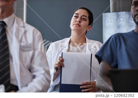 Medium shot of thoughtful Middle Eastern female physician attending lecture at conference room taking continuing learning course at hospital, copy space 120682302