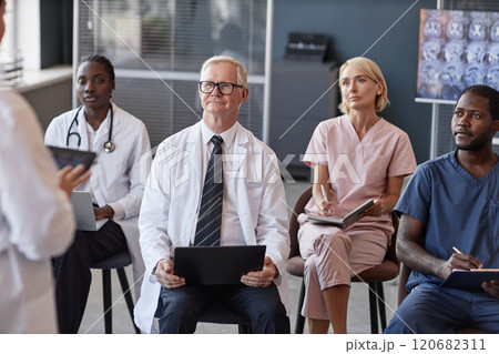 Senior male head physician listening to colleagues presentation with diverse team of doctors while participating in seminar at conference room 120682311