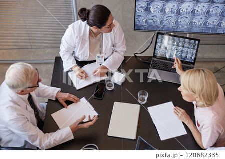 High angle shot of Middle Eastern female radiologist sitting at meeting table, while colleague pointing at laptop screen with X ray scan of brain speculating on patients condition at medical office High angle shot of Middle Eastern female radiologist sitting at meeting table, while colleague pointing at laptop screen with X ray scan of brain speculating on patients condition at medical office 120682335