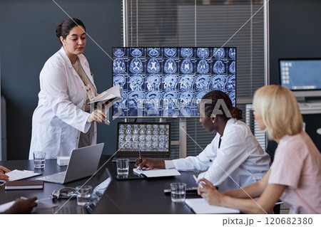 Professional female radiologist of Middle Eastern ethnicity showing MRI scan images of patients brain on screen, presenting research results to colleagues at board meeting at medical office Professional female radiologist of Middle Eastern ethnicity showing MRI scan images of patients brain on screen, presenting research results to colleagues at board meeting at medical office 120682380