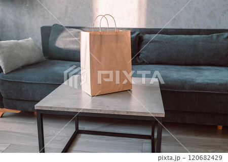 Disposable bag of kraft paper with products left by courier of food delivery service on a table at home. Copy space. Kraft design. Disposable bag of kraft paper with products left by courier of food delivery service on a table at home. Copy space. Kraft design. 120682429