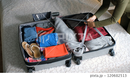 In a cozy room, young woman organizes her suitcase, folding clothes and arranging essentials for her trip 120682513