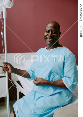 Smiling African American patient sitting on hospital bed, holding IV stand with room background 120683572