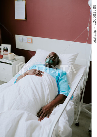 Senior African American man resting in hospital bed wearing oxygen mask, displaying medical equipment and clipboard on wall Senior African American man resting in hospital bed wearing oxygen mask, displaying medical equipment and clipboard on wall 120683589