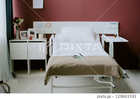 Empty hospital bed with medical equipment and a nightstand in a clean, well-lit room with beige walls, displaying a serene and orderly atmosphere 120683591