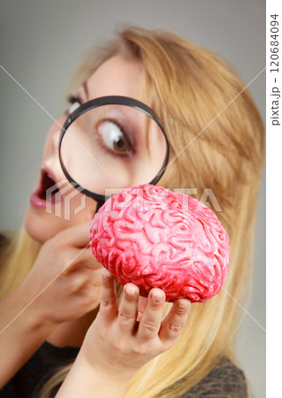Woman holding magnifying glass investigating brain 120684094