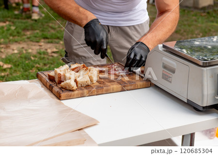 cutting bread and ham into cubes for tasting, knife in hand 120685304