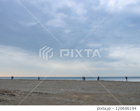 Small silhouettes of people on the shore. People in the distance stand and look at the sea. Overcast weather. Out of season at the 120686194
