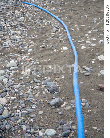 Cable on black sand. The cable sticks out of the ground. Electrical communications on the beach. Industry. 120686235