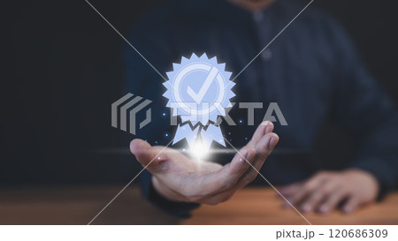 A businessman holds a glowing digital certification badge with a checkmark symbol, representing quality, trust, and achievement. The futuristic design highlights success and recognition. A businessman holds a glowing digital certification badge with a checkmark symbol, representing quality, trust, and achievement. The futuristic design highlights success and recognition. 120686309