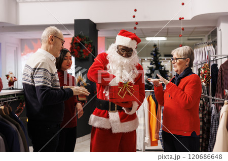 Worker drawing raffle winners names in shop, presenting participants from red contest box. African american person in santa claus red suit greeting clients at prize drawing activity. Worker drawing raffle winners names in shop, presenting participants from red contest box. African american person in santa claus red suit greeting clients at prize drawing activity. 120686648