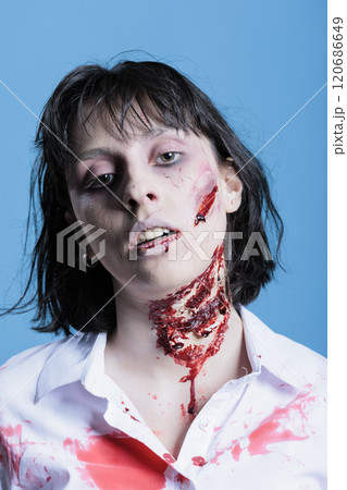 Portrait of creepy woman covered in blood, turning into zombie after being killed. Undead cadaver filled with scars, possessed by demon, turning into feral ghoul, studio background Portrait of creepy woman covered in blood, turning into zombie after being killed. Undead cadaver filled with scars, possessed by demon, turning into feral ghoul, studio background 120686649