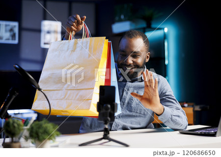 Content creator does influencer marketing, unboxing bags with internet order, showing subscribers purchases he recently got. Man presenting fans shopping acquisitions product placement Content creator does influencer marketing, unboxing bags with internet order, showing subscribers purchases he recently got. Man presenting fans shopping acquisitions product placement 120686650