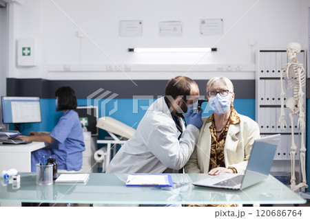 Young doctor inspects ear of female pensioner patient with professional care, checking for infection using otology equipment. Male physician holds otoscope and performs hearing test on retired woman. 120686764