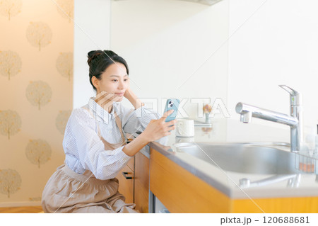 キッチンでスマホを見る女性 120688681