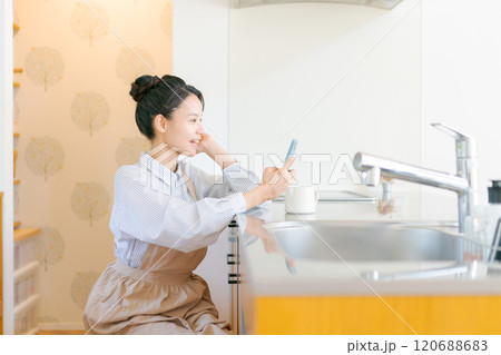 キッチンでスマホを見る女性 120688683