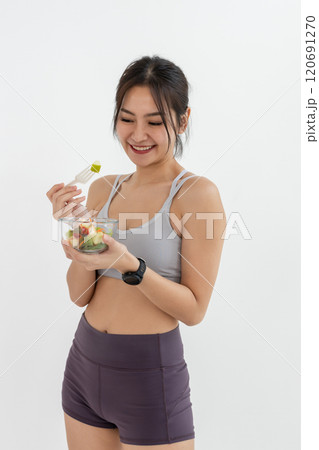 Asian attractive lady sportswear healthy eating salad vegetables over white background. Female holding salad bowl various vegetables and fruit healthy food for weight loss and exercise. 120691270