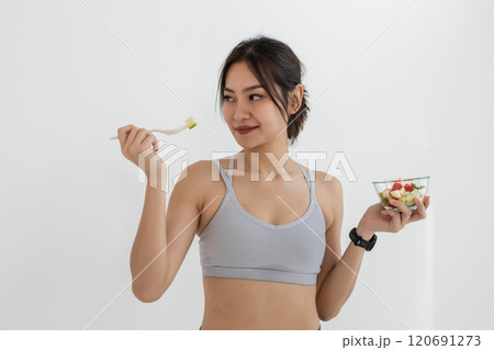 Asian attractive lady sportswear healthy eating salad vegetables over white background. Female holding salad bowl various vegetables and fruit healthy food for weight loss and exercise. 120691273