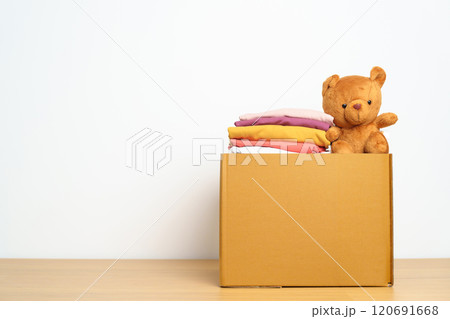 Kid Donation, Charity, Volunteer, Giving and Delivery Concept. Hand donate Bear doll and Clothes into cardboard box at home for support and help poor, refugee and homeless people. Copy space for text 120691668
