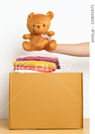 Kid Donation, Charity, Volunteer, Giving and Delivery Concept. Hand donate Bear doll and Clothes into cardboard box at home for support and help poor, refugee and homeless people. Copy space for text 120691671