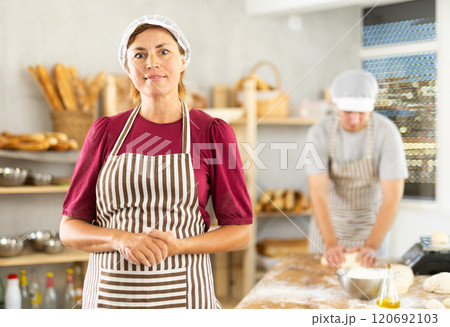 In working room of bakery, there is woman with baguettes in wicker basket in hands In working room of bakery, there is woman with baguettes in wicker basket in hands 120692103