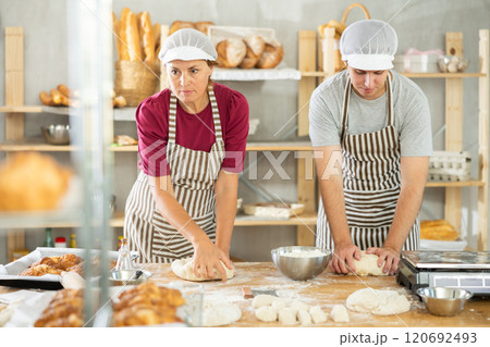 Two bakers, woman and young guy, knead raw dough on table in bakery kitchen 120692493