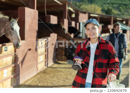 Cheerful female holding brushes for grooming horses outdoors Cheerful female holding brushes for grooming horses outdoors 120692670