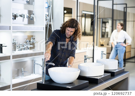 in plumbing department,thoughtful man inspects round white ceramic sinks with faucets 120692737