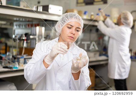 Concentrated young woman scientist doing experiment with petri dish 120692959