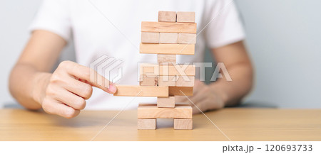 hand pulling wooden block tower on table. Business planning, Risk Management, Solution, leader, strategy, Crisis, falling Business, and Economic recession concept hand pulling wooden block tower on table. Business planning, Risk Management, Solution, leader, strategy, Crisis, falling Business, and Economic recession concept 120693733