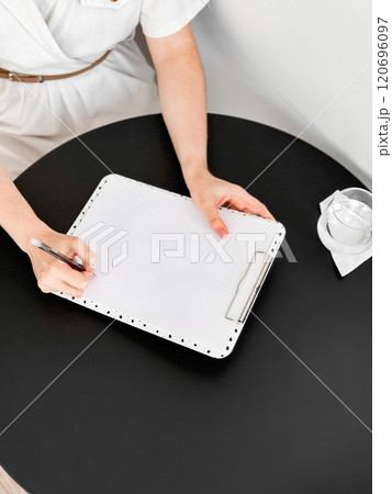 Person writing on blank paper clipboard at round black table meeting Person writing on blank paper clipboard at round black table meeting 120696097