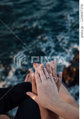 Female and male hand with rings together on a sea rock Female and male hand with rings together on a sea rock 120697356