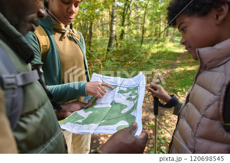 Medium close up of paper map in hands of unrecognizable father, his son and daughter looking at it 120698545